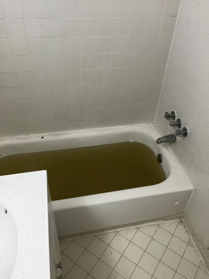 Bathtub filled with murky brown water, next to a white sink in a tiled bathroom.