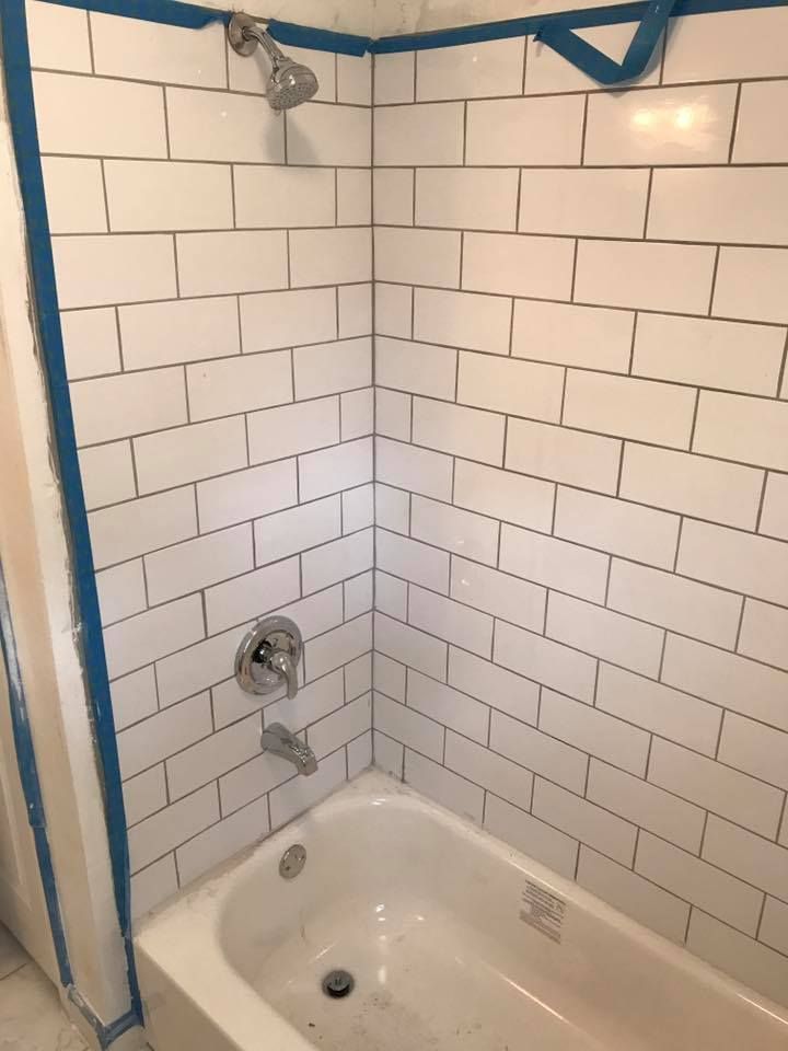White tiled shower and tub with chrome fixtures, blue tape trim.