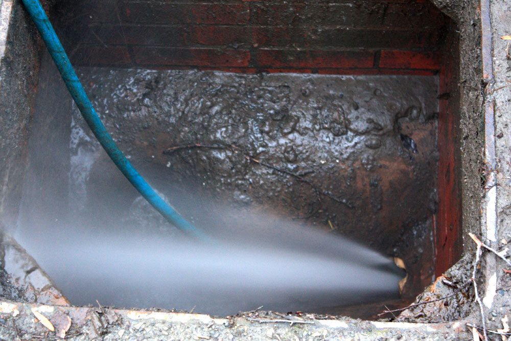 A person washes a gray garage door with a pressure washer.