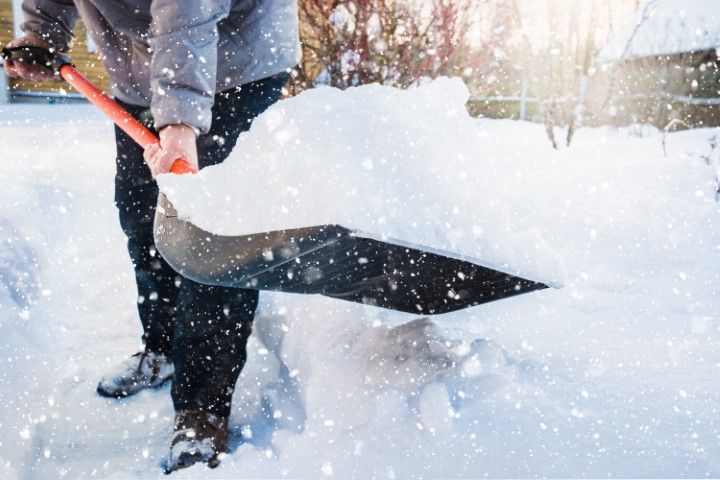 A man is holding a shovel to sweep out the snow outside his house.