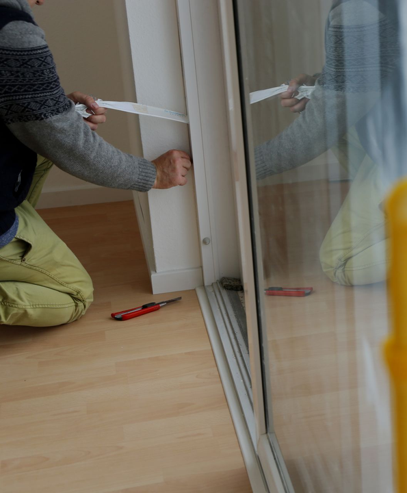 Mann kniet am Boden und baut Terrassentür ein