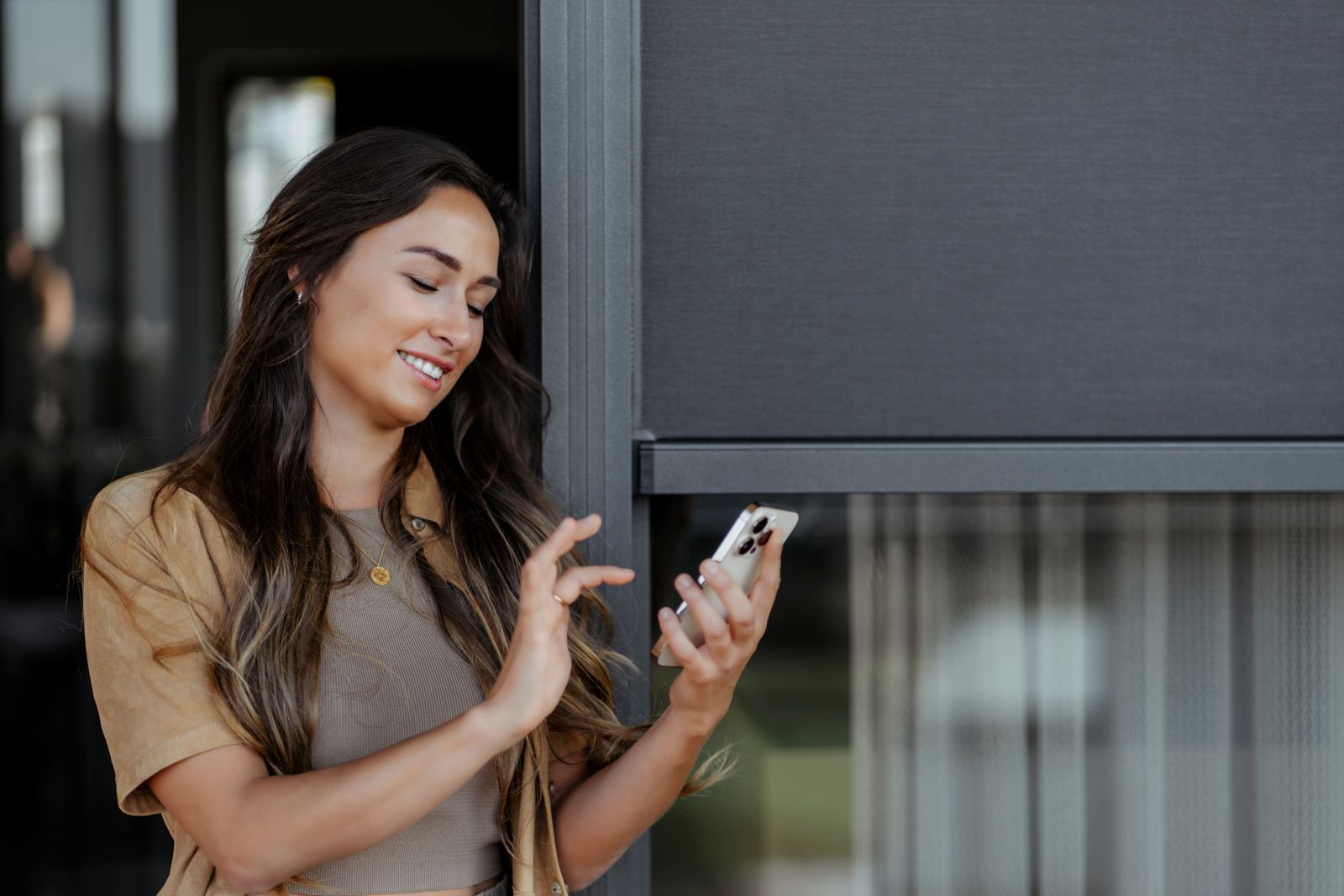 Person in einem hellbraunen Hemd lächelt, während sie mit smartphone den Sonnenschutz regelt