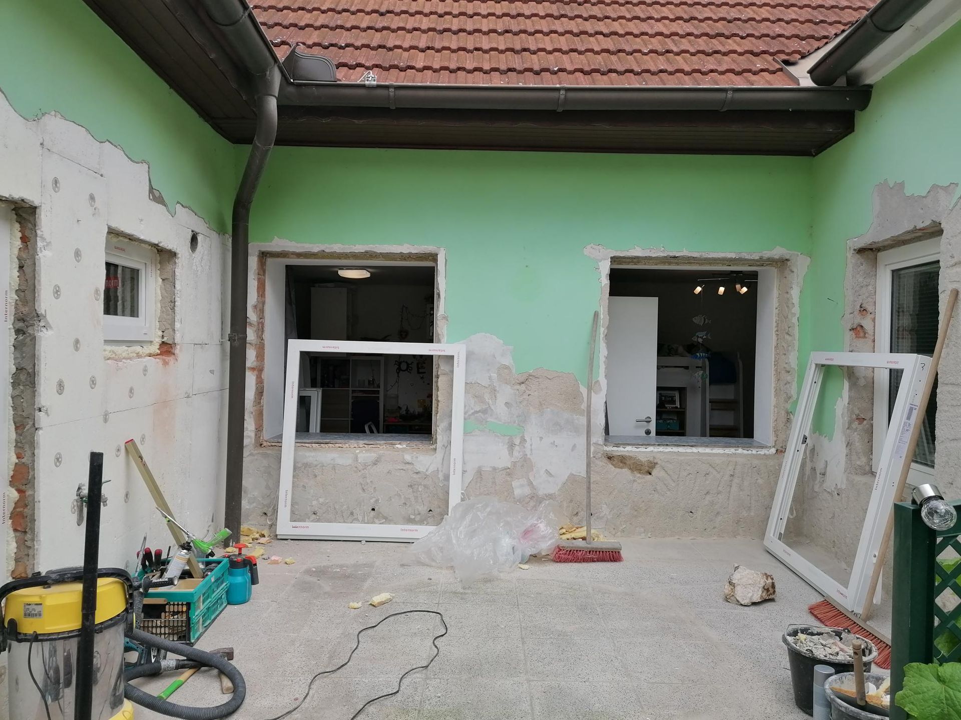 Fassade eines Gebäudes, das derzeit renoviert wird, mintgrüne Wände und an die Wand gelehnte  neue Fensterrahmen.