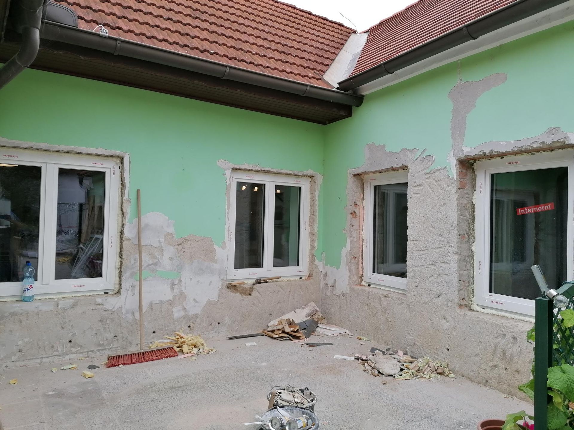 Eine L-förmige Gebäudefassade mit hellgrünen, derzeit sanierten Wänden und vier neuen, weiß gerahmten Fenstern.