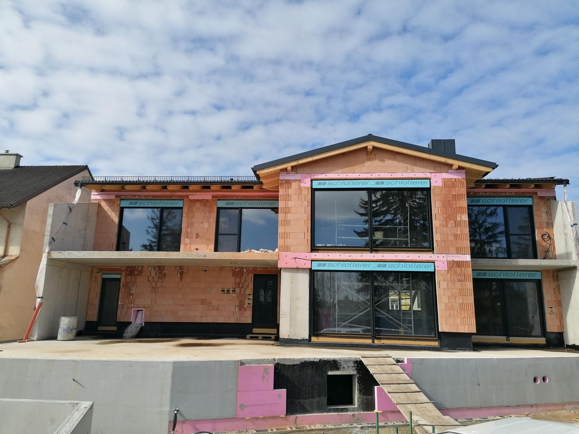 Ein modernes, zweistöckiges Haus im Bau mit großen Fenstern, unfertigen Außenwänden und einer Betonterrasse.