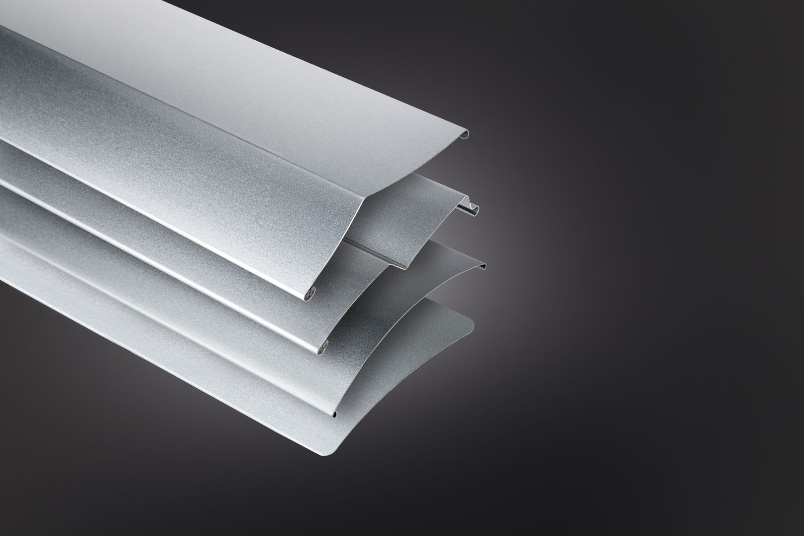 Gestapelte silberne Metalllamellen mit einem geschwungenen, gerillten Design vor dunklem Hintergrund.