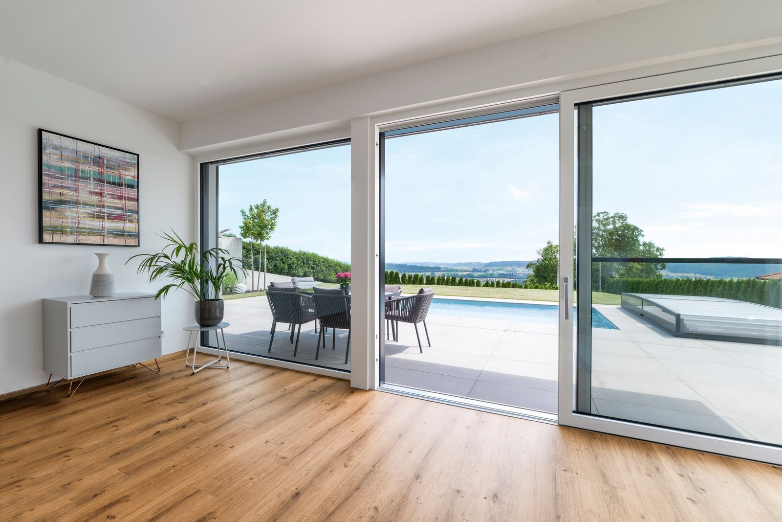 helles Zimmer mit Holzboden und Kommode, das sich zu einer Terrasse mit Swimmingpool öffnet.
