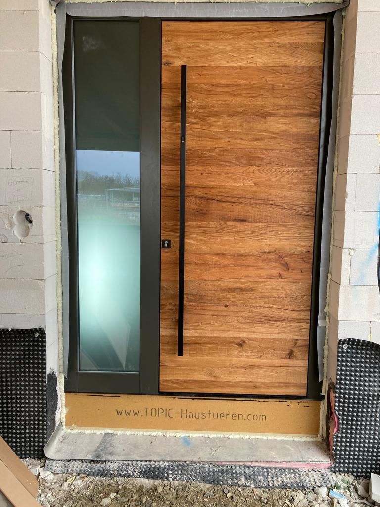 moderne, holzgetäfelte Eingangstür mit hohem, schwarzem Griff und seitlicher Glasscheibe