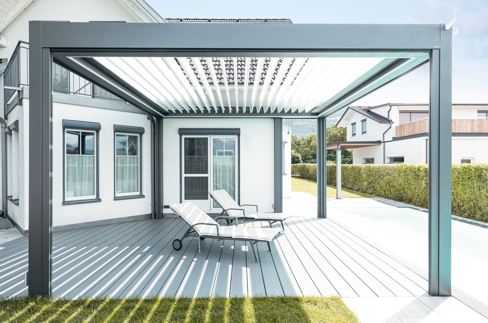 Zwei Liegestühle auf einer grauen Terrasse unter einer modernen, dunkelgrauen Pergola mit verstellbarem Lamellendach.