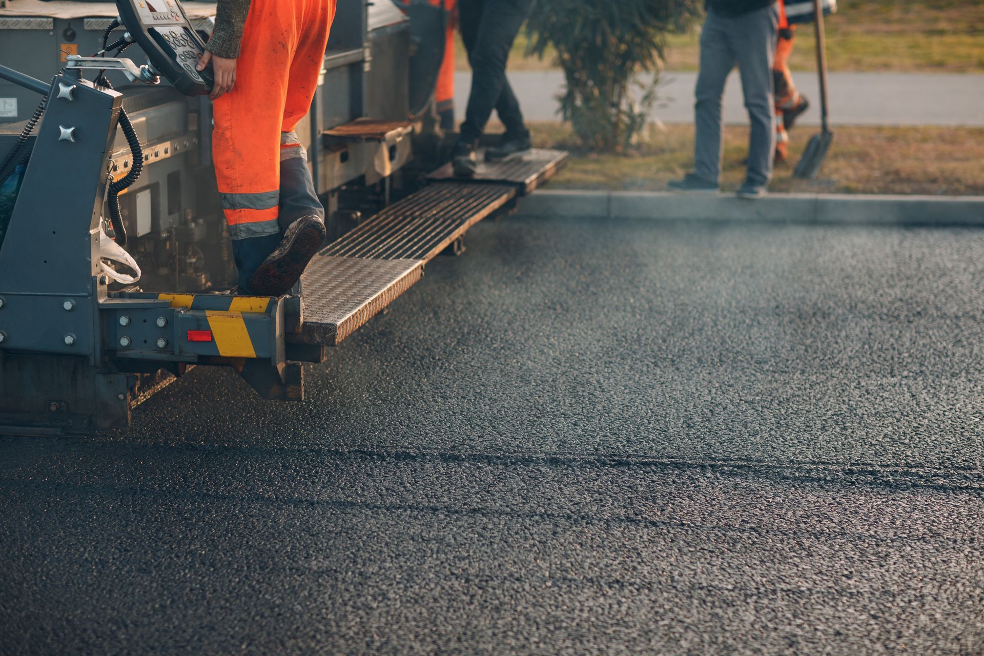 Road paving machine laying fresh asphalt with workers nearby.
