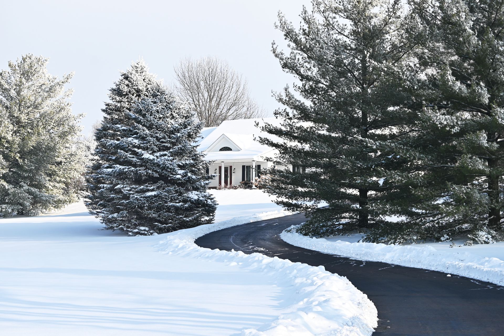A snowy asphalted road winding through a winter landscape, leading to a cozy house in the distance.