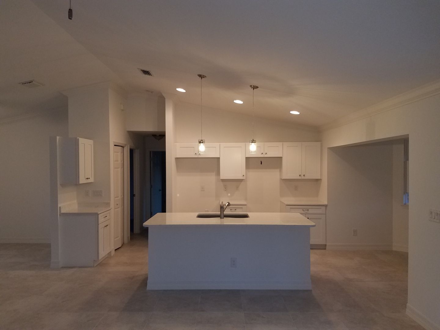 An empty kitchen with white cabinets and a large island built by Blue Heron Construction Cape Coral