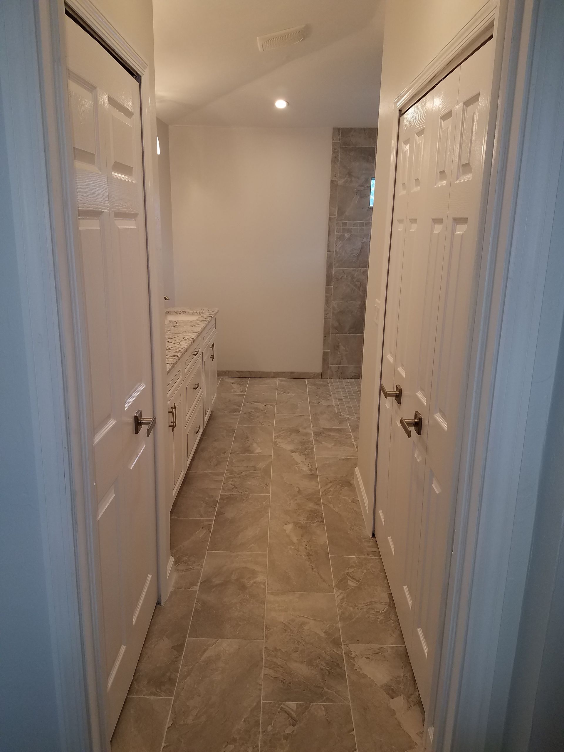 A long hallway with white doors and tile floors leading to a bathroom.
