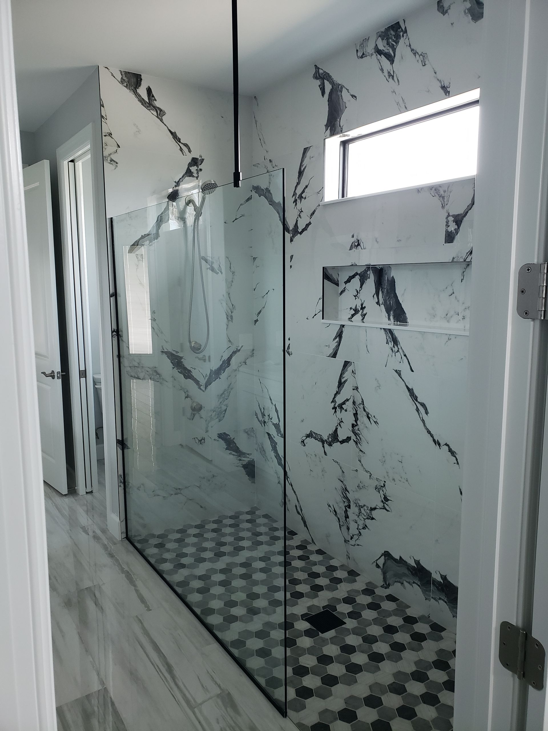 A bathroom with a walk in shower with a marble wall.