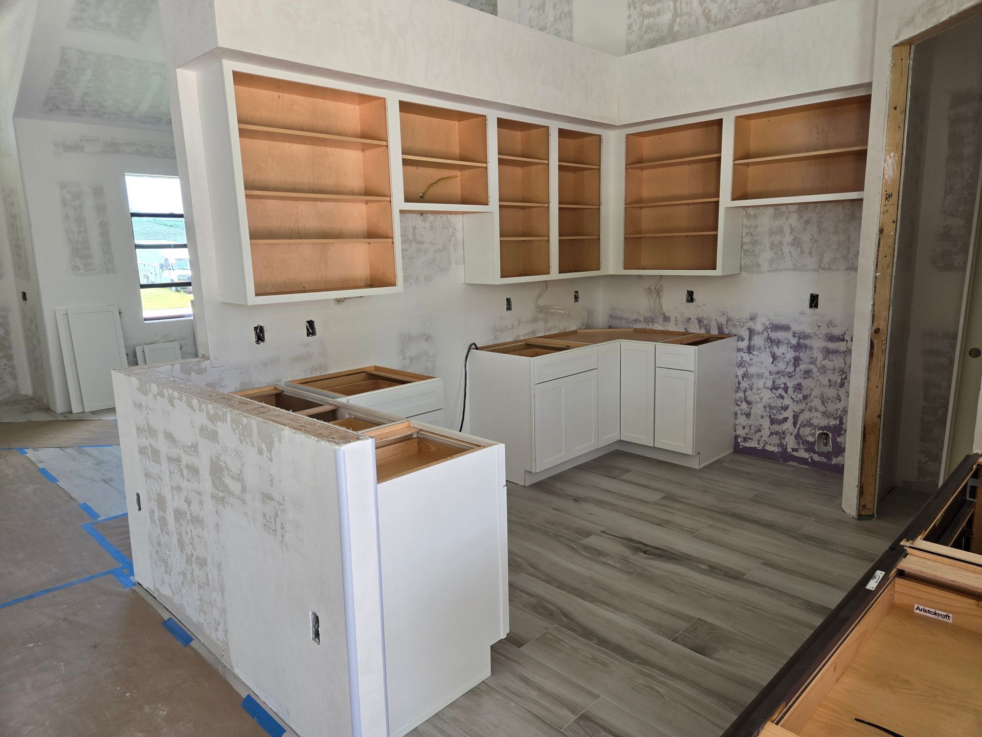 A kitchen under construction with white cabinets and wooden floors.