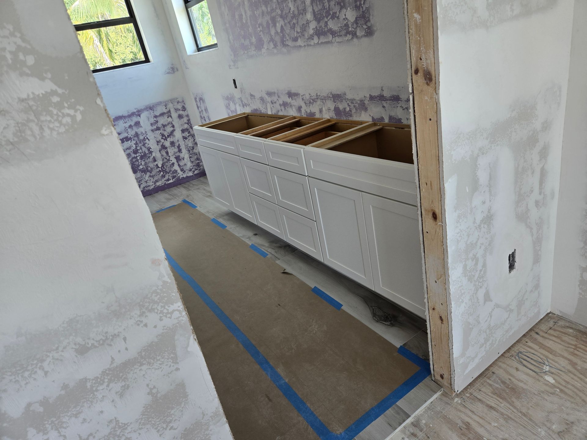 A bathroom under construction with white cabinets and blue tape on the floor
