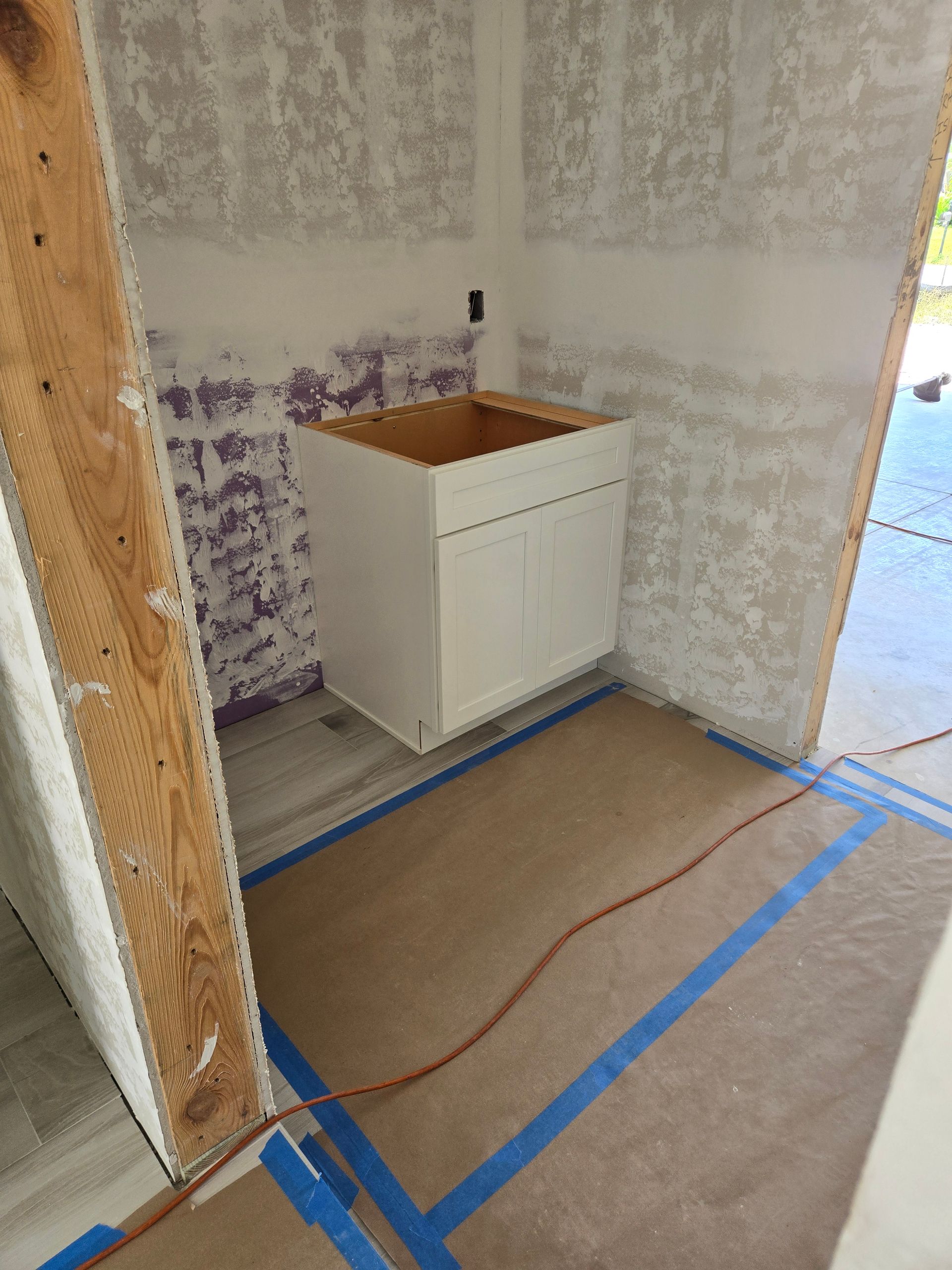 A bathroom under construction with a sink and blue tape on the floor.