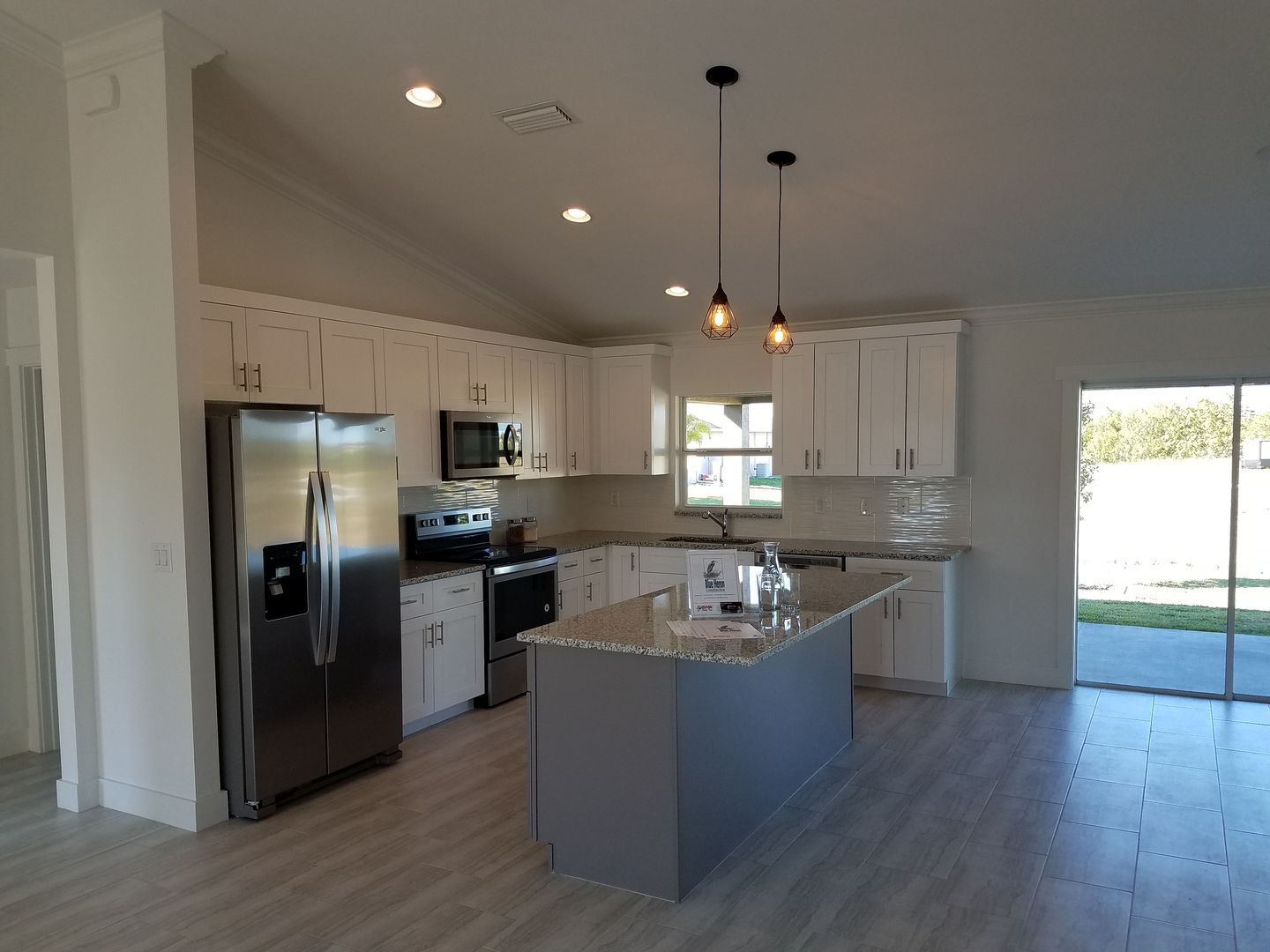 A kitchen with white cabinets , stainless steel appliances , and a large island built by Blue Heron Construction Cape Coral