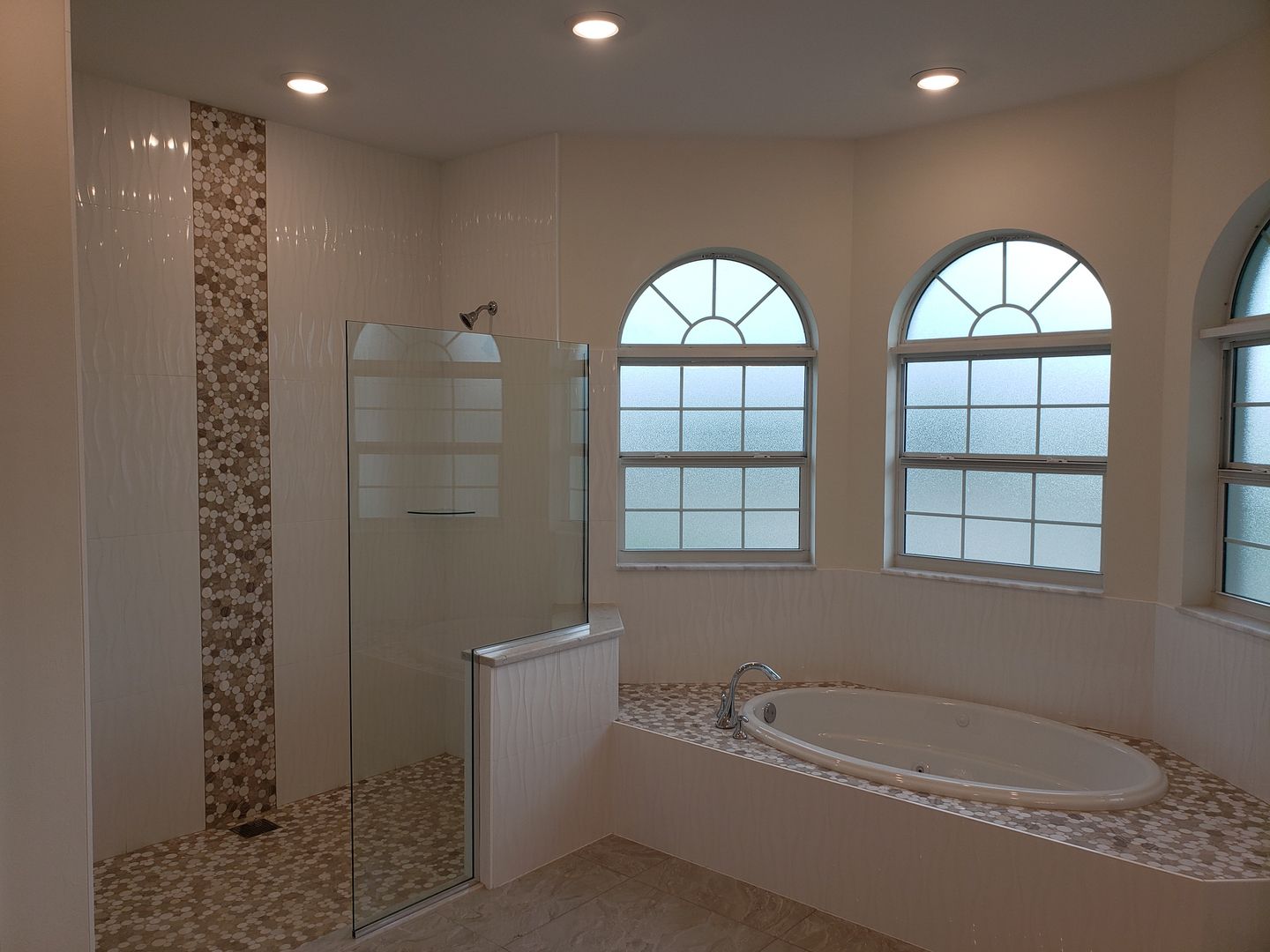A bathroom with a tub and a shower with arched windows built by Blue Heron Construction Cape Coral