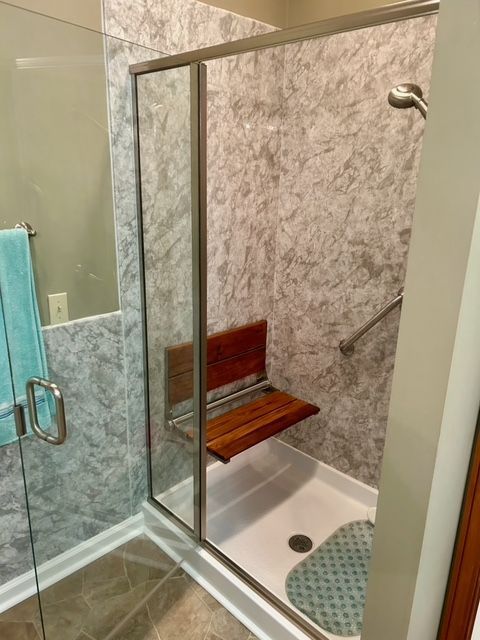 A bathroom with a walk in shower with a wooden seat.