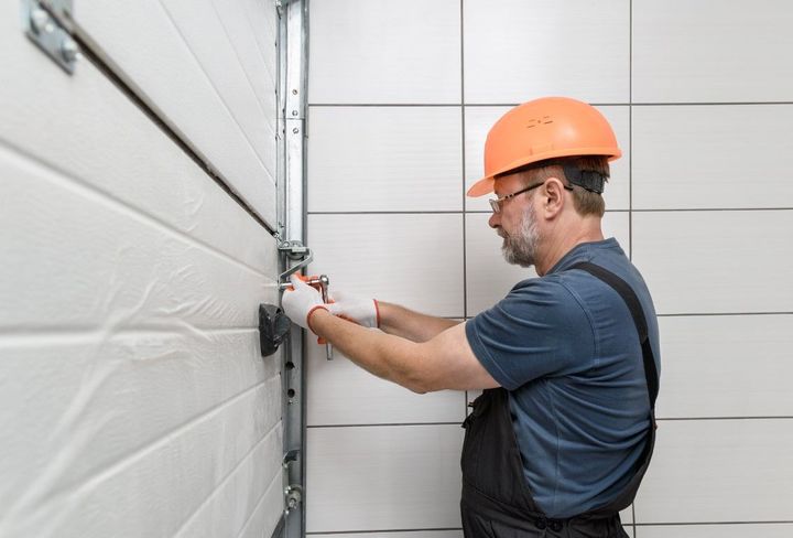 A man wearing a hard hat is working on a garage door.