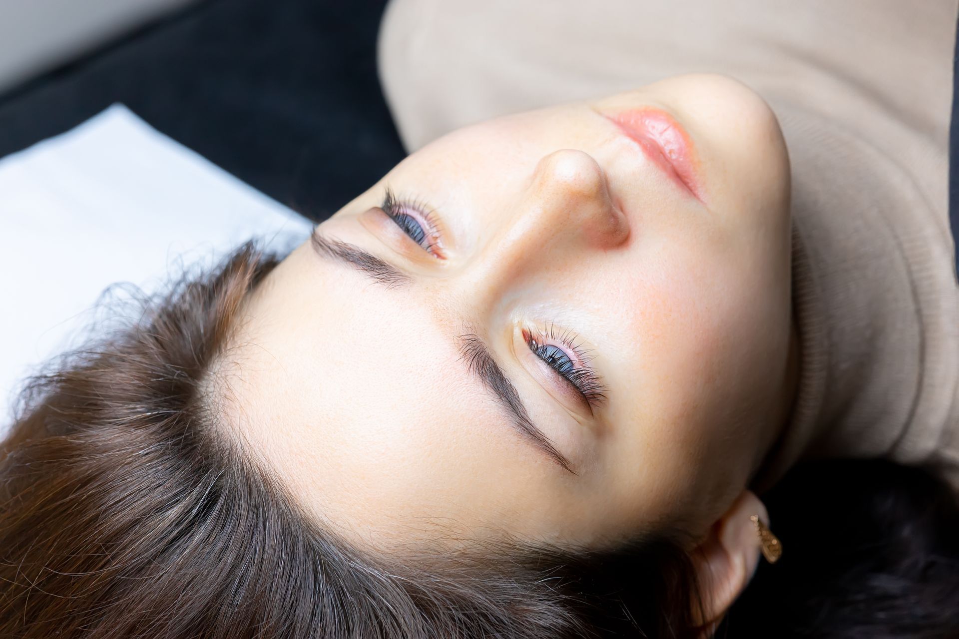 Woman with work being done on her eyebrows, lying down with eyes closed.