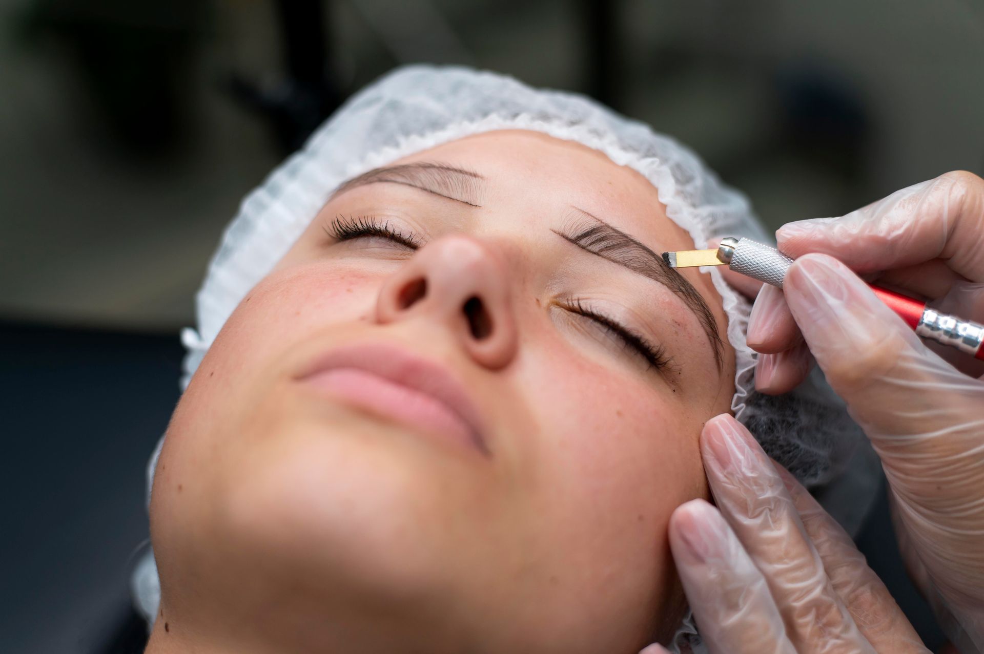 A woman is getting her eyebrows tattooed with a machine.