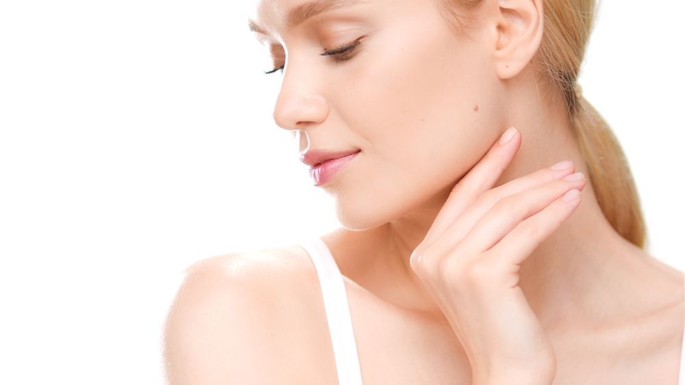 Blonde woman with eyes closed, hand touching neck; white tank top and background.