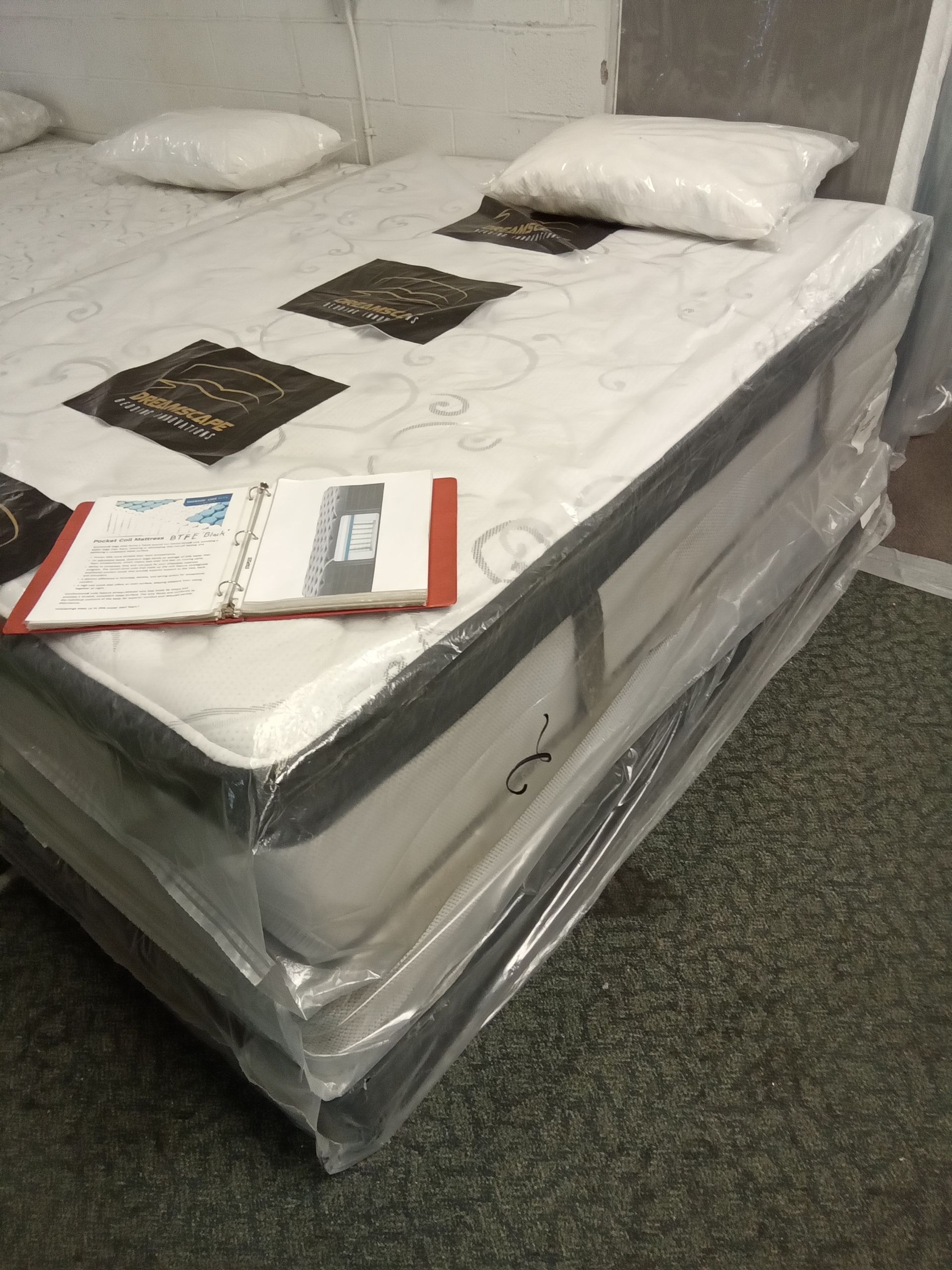 A mattress is wrapped in plastic and has a book on top of it.