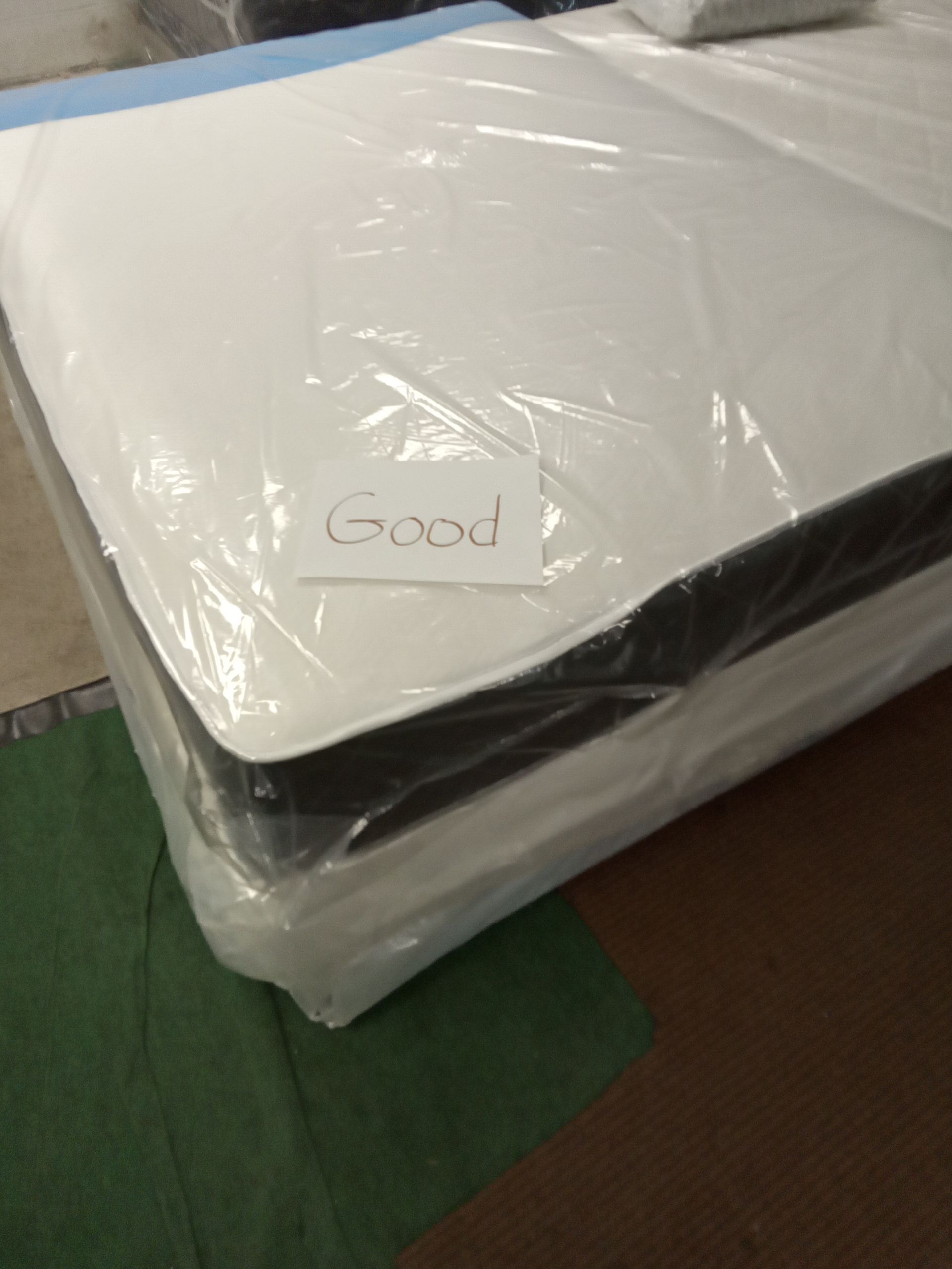 A mattress is wrapped in plastic and has the word good written on it