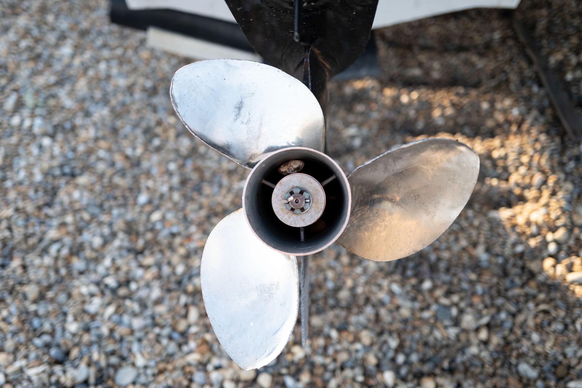 A close up of a propeller on a boat on gravel.