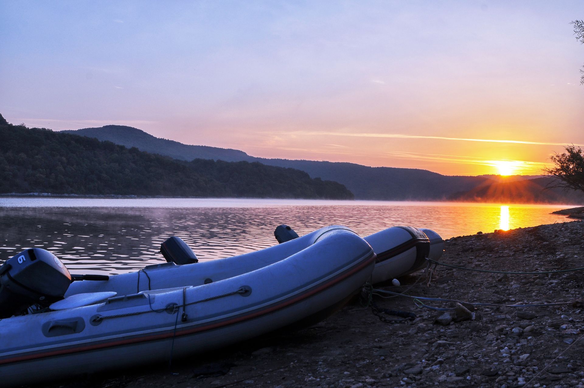 Two boats are on the shore of a lake at sunset