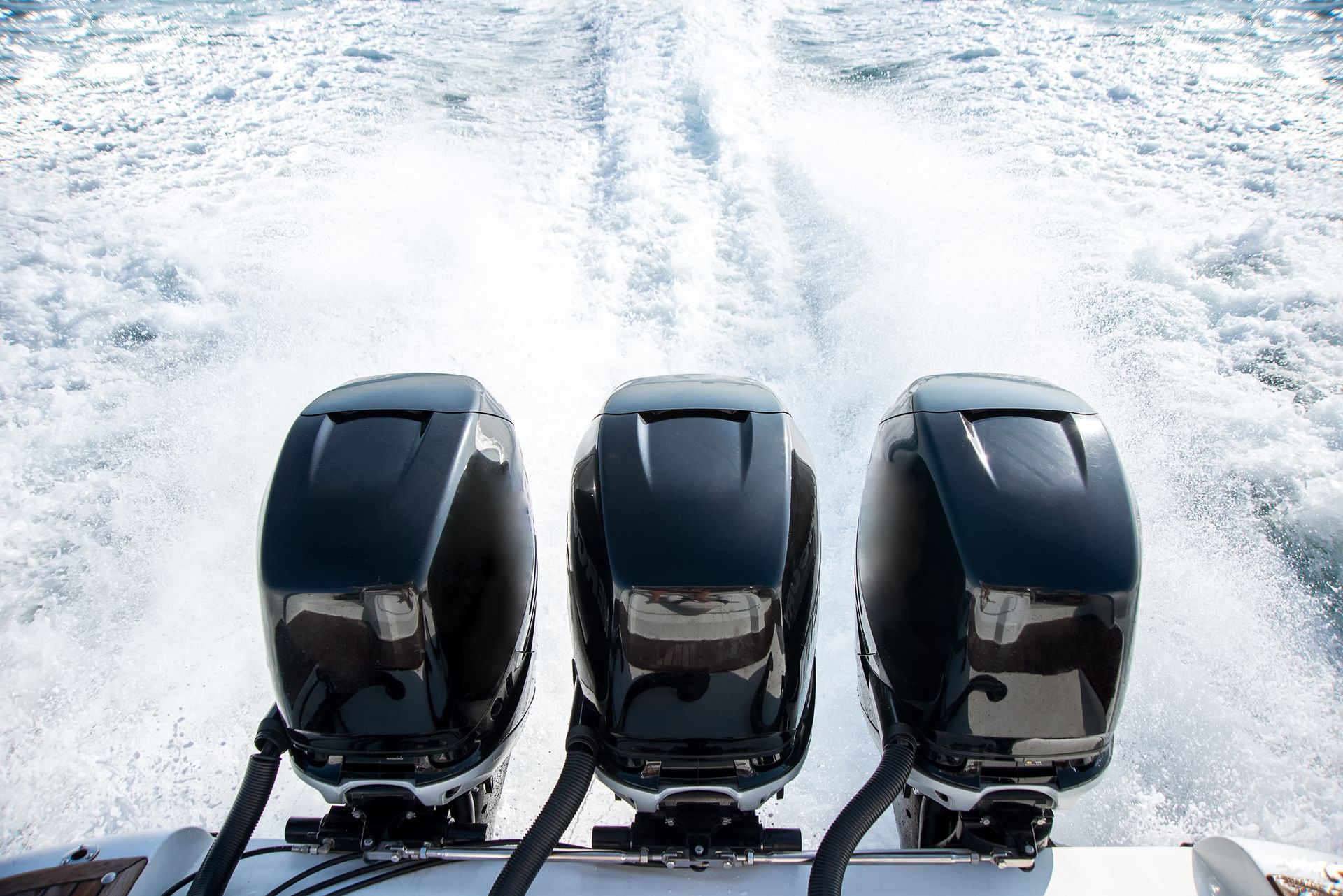 Three outboard motors are driving a boat in the ocean.