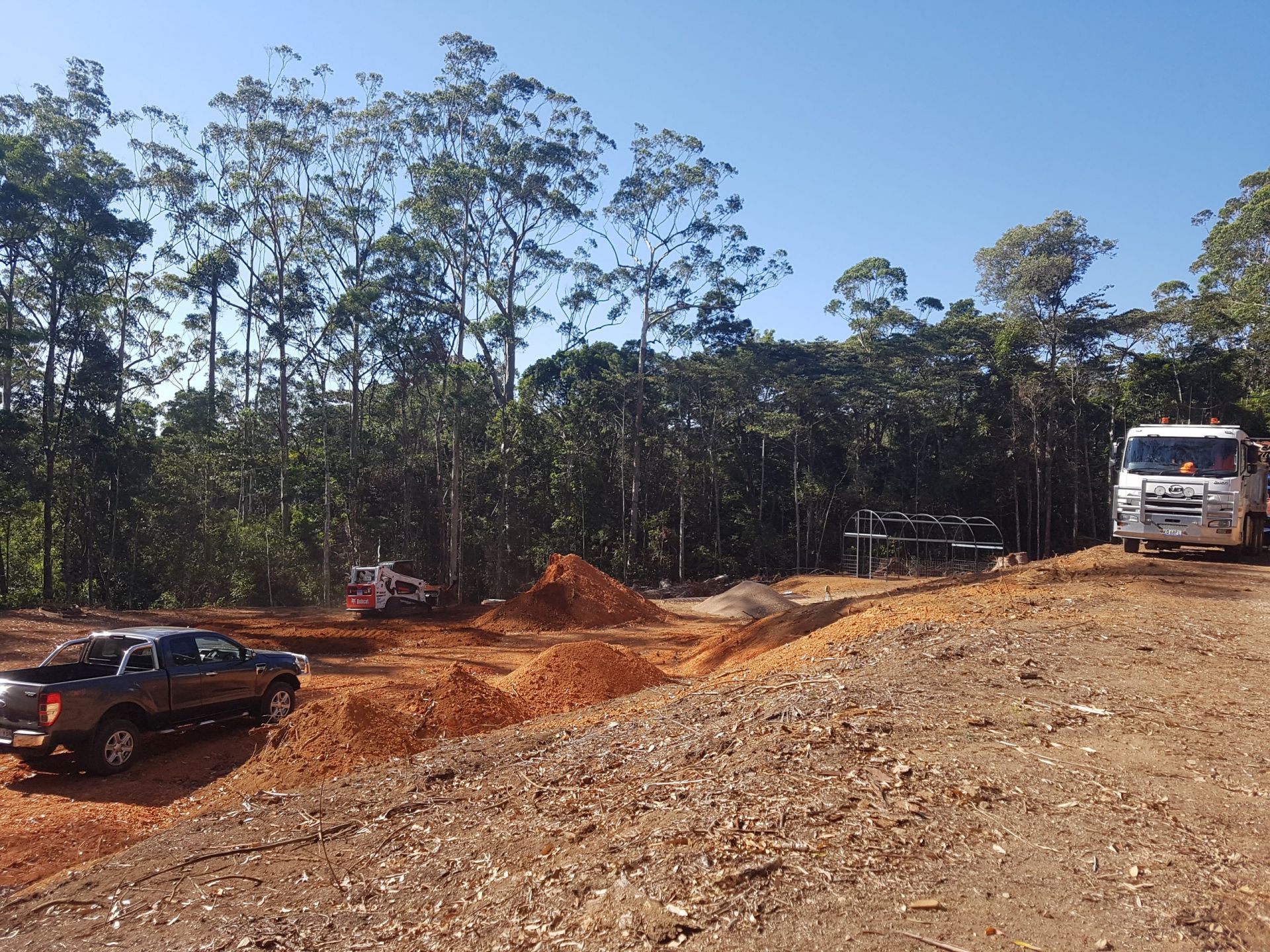 Dirt Road with Construction Vehicles and Piles of Dirt in A Forested Area — Evans Earthmoving Contractors In Malanda, QLD