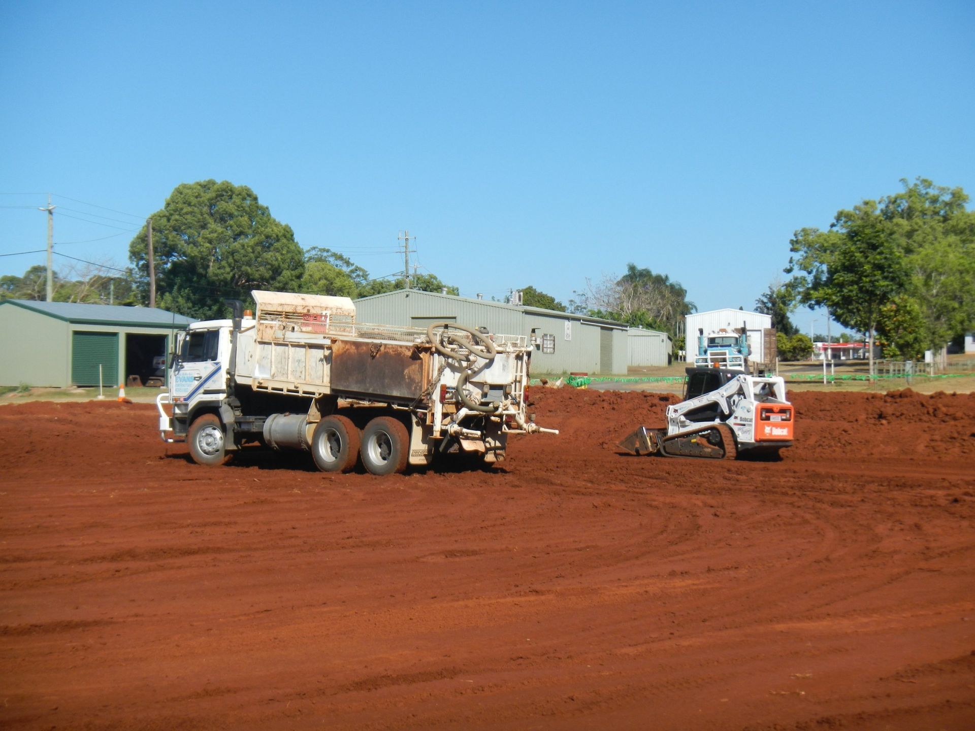 A Dump Truck and A Skid Steer Working on A Large Area of Red Dirt Under a Blue Sky — Evans Earthmoving Contractors In Malanda, QLD