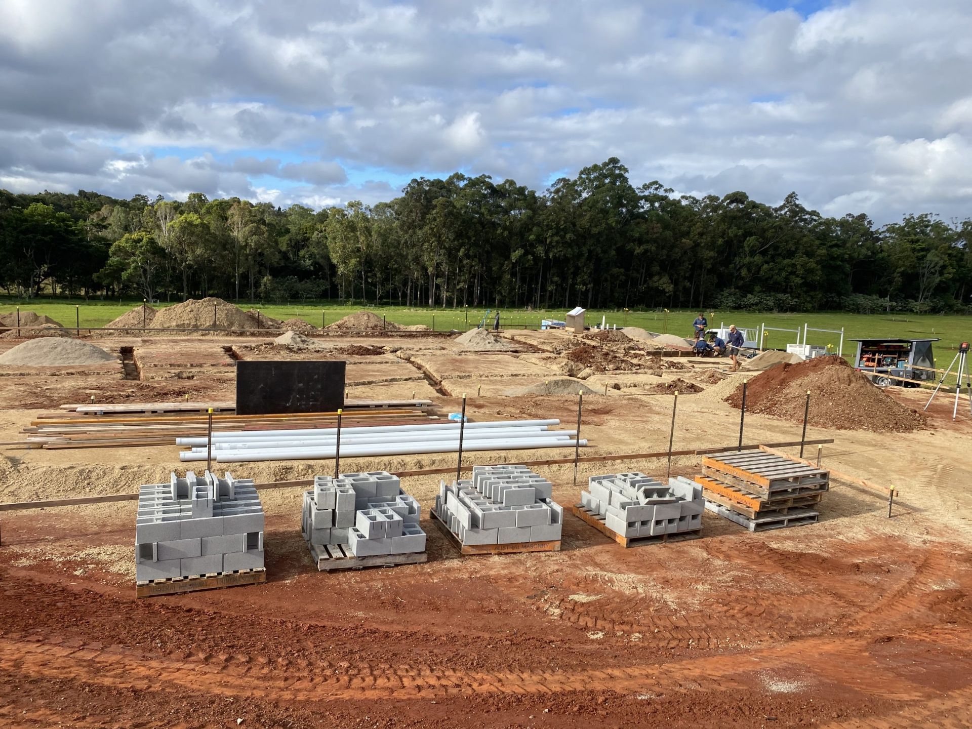 Construction Site with Piles of Concrete Blocks and Wood, Surrounded by Dirt and A Grassy Field with Trees — Evans Earthmoving Contractors In Malanda, QLD