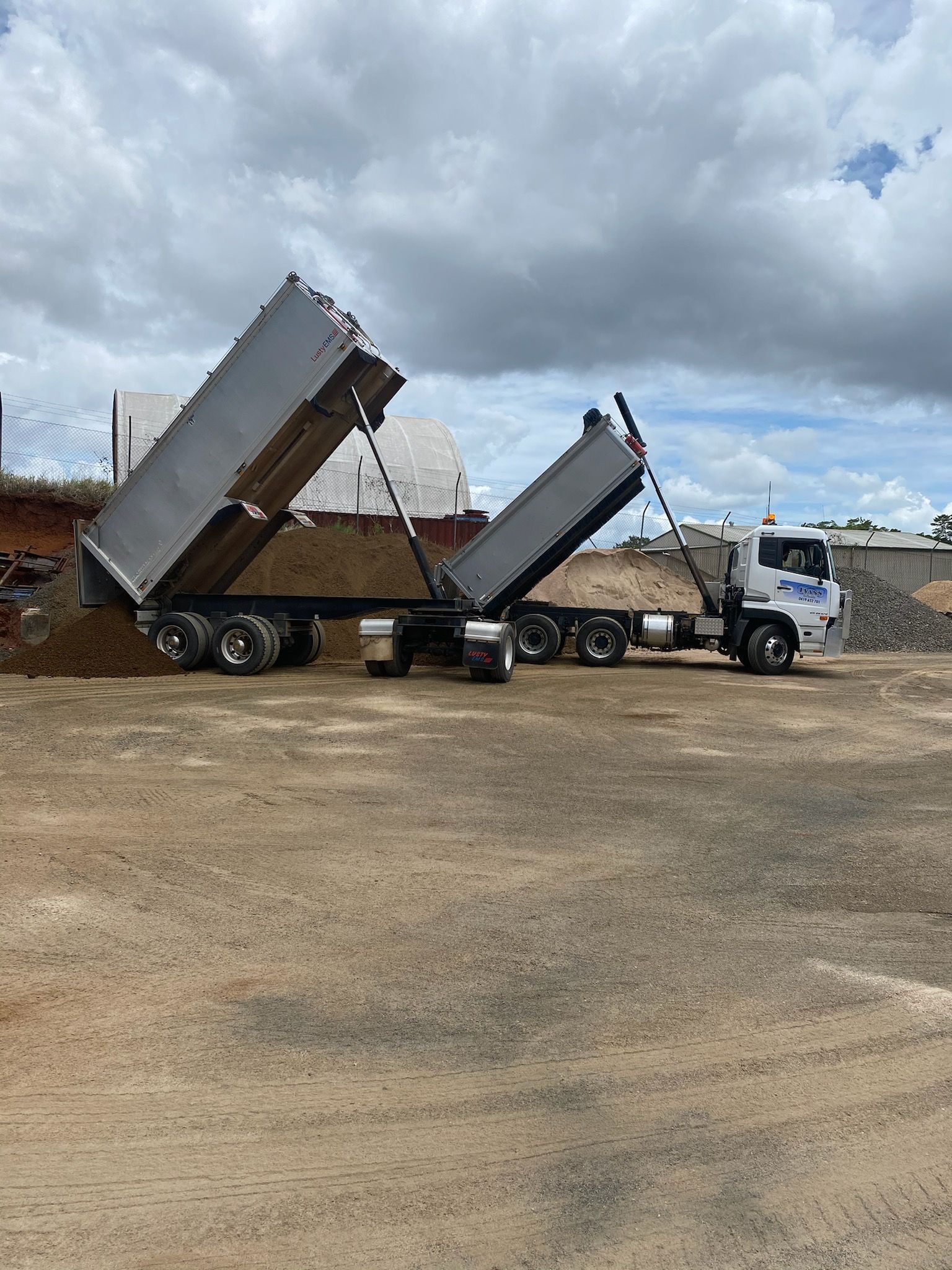 Two Raised Dump Truck Beds at a Gravel Lot Under Cloudy Skies — Evans Earthmoving Contractors In Mareeba, QLD