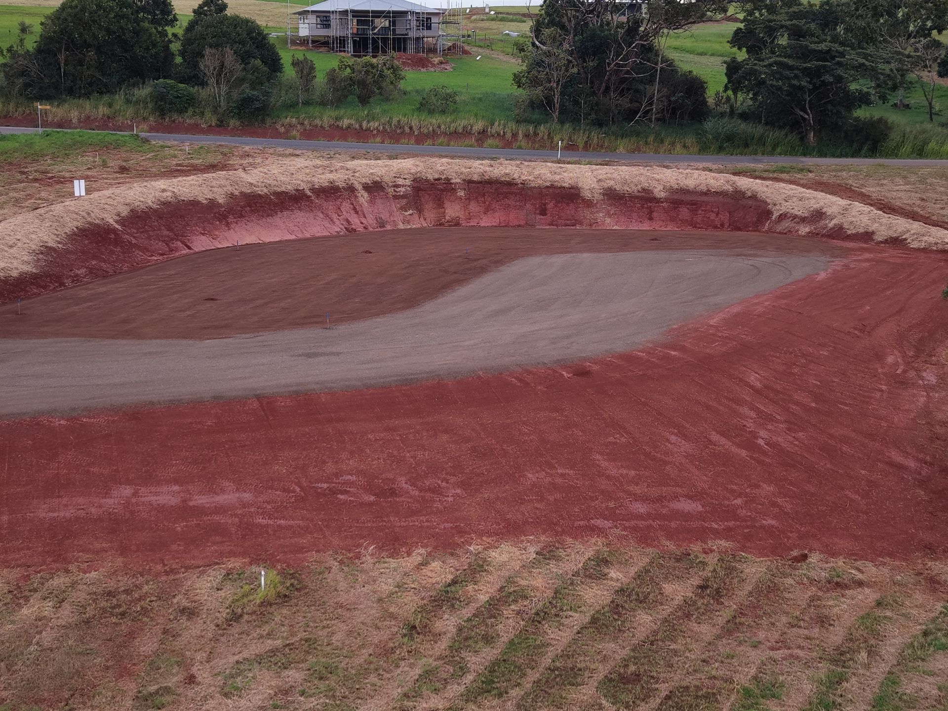Freshly graded red dirt field with a gray center, bordered by grass and trees in the background — Evans Earthmoving Contractors In Malanda, QLD 