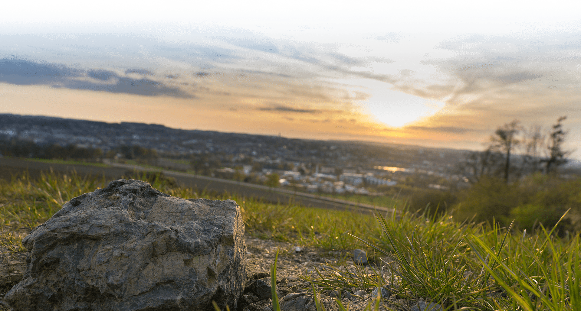 Sunset Over a Town from A Grassy Hillside; Large Rock in The Foreground — Evans Earthmoving Contractors In Malanda, QLD