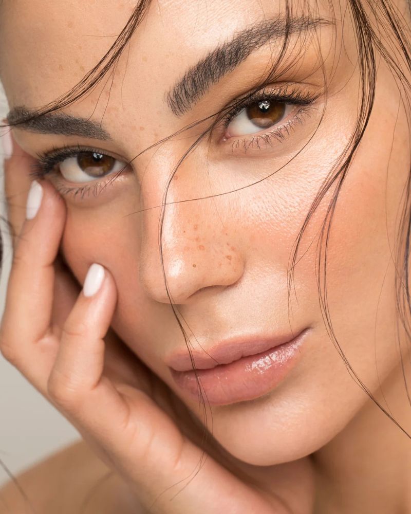 Ein Schwarzweißfoto des Gesichts einer Frau neben einer Flasche Microneedling-Stift.