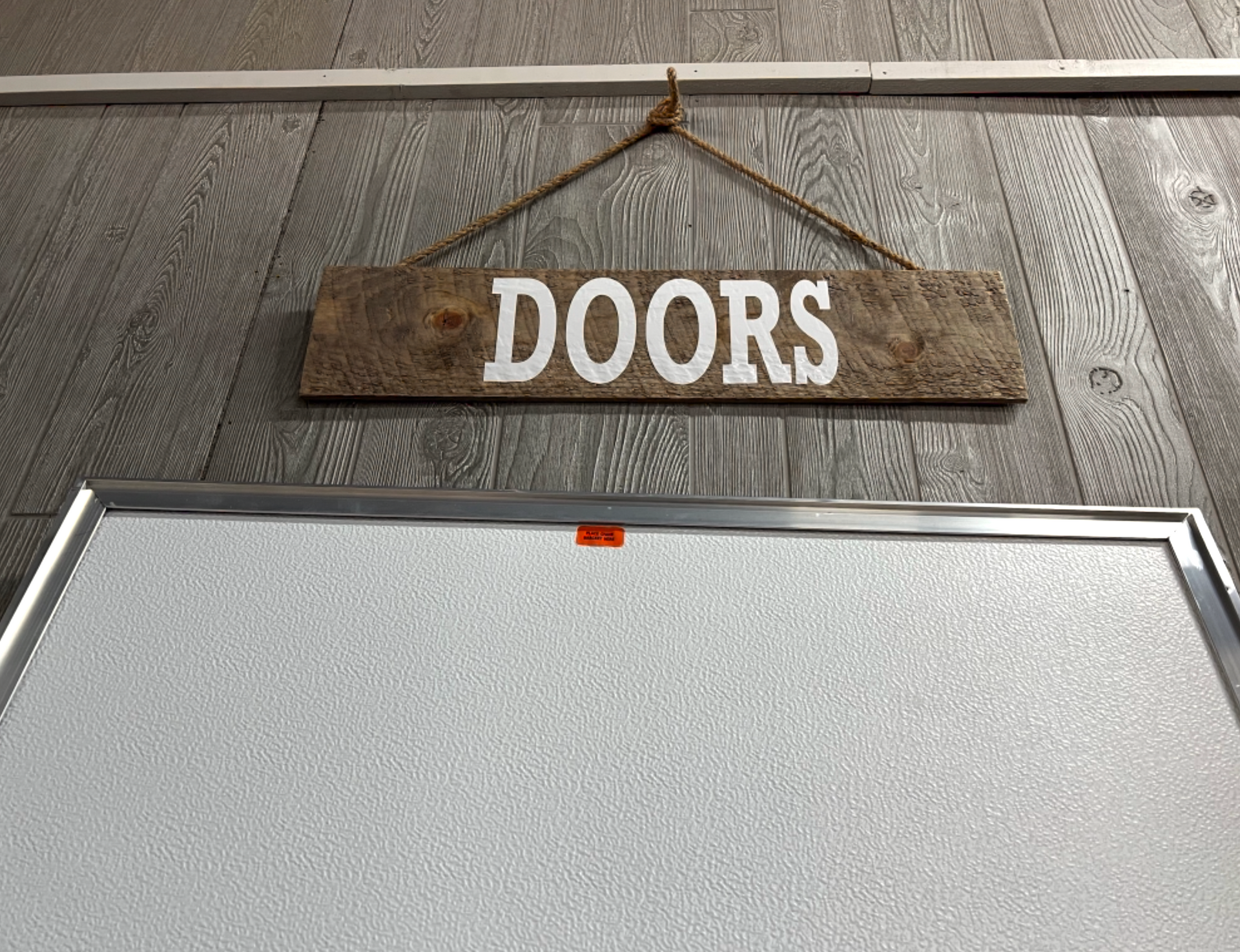 A sign that says doors is hanging on a wooden wall next to a white board.