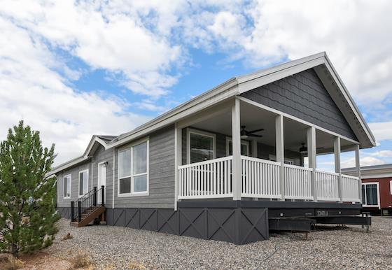 Modern double-wide manufactured home with covered front porch, gray siding, and gravel yard setting.
