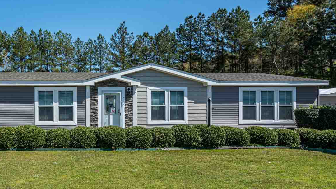 A mobile home with a lot of windows is sitting on top of a lush green field.