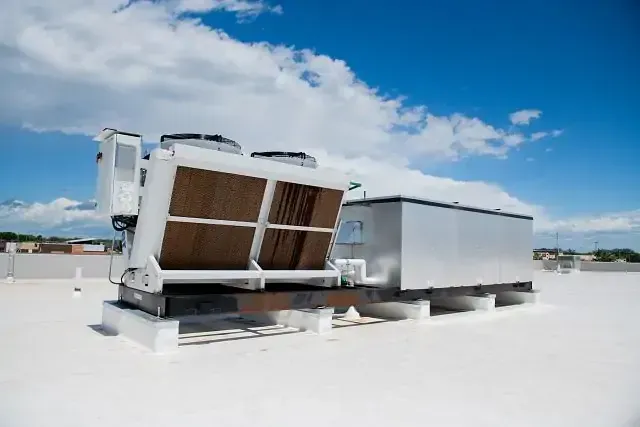White rooftop HVAC units on a flat roof under a blue sky with clouds