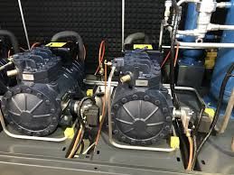 Two black industrial air compressors mounted on a metal base with hoses and valves in a utility room