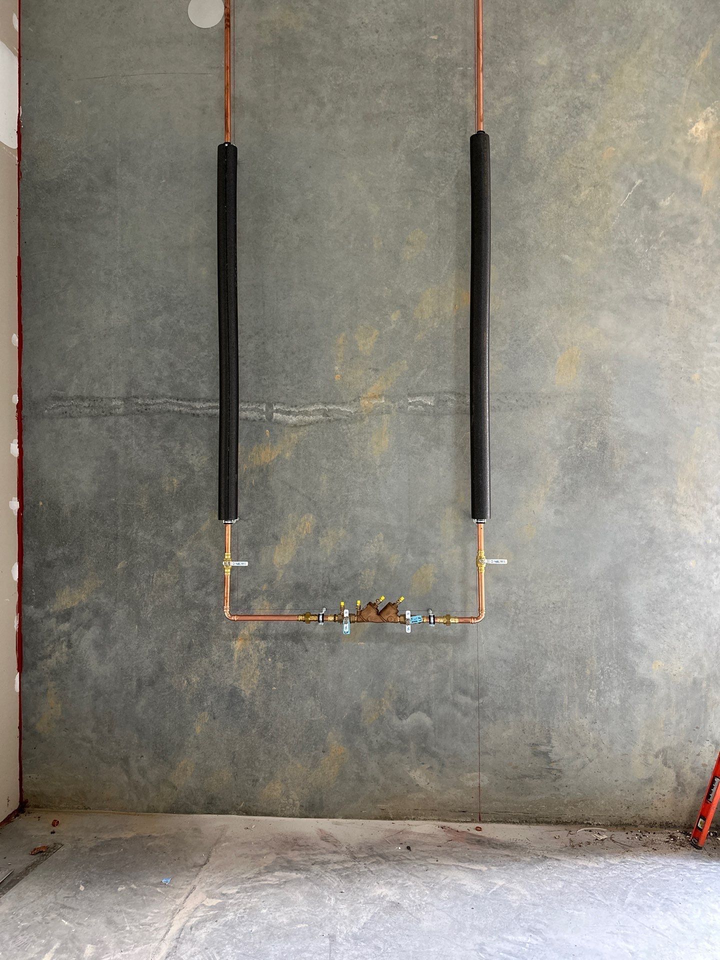 Copper plumbing pipes on a gray wall, forming a U-shape. Black insulation covers the vertical pipes.