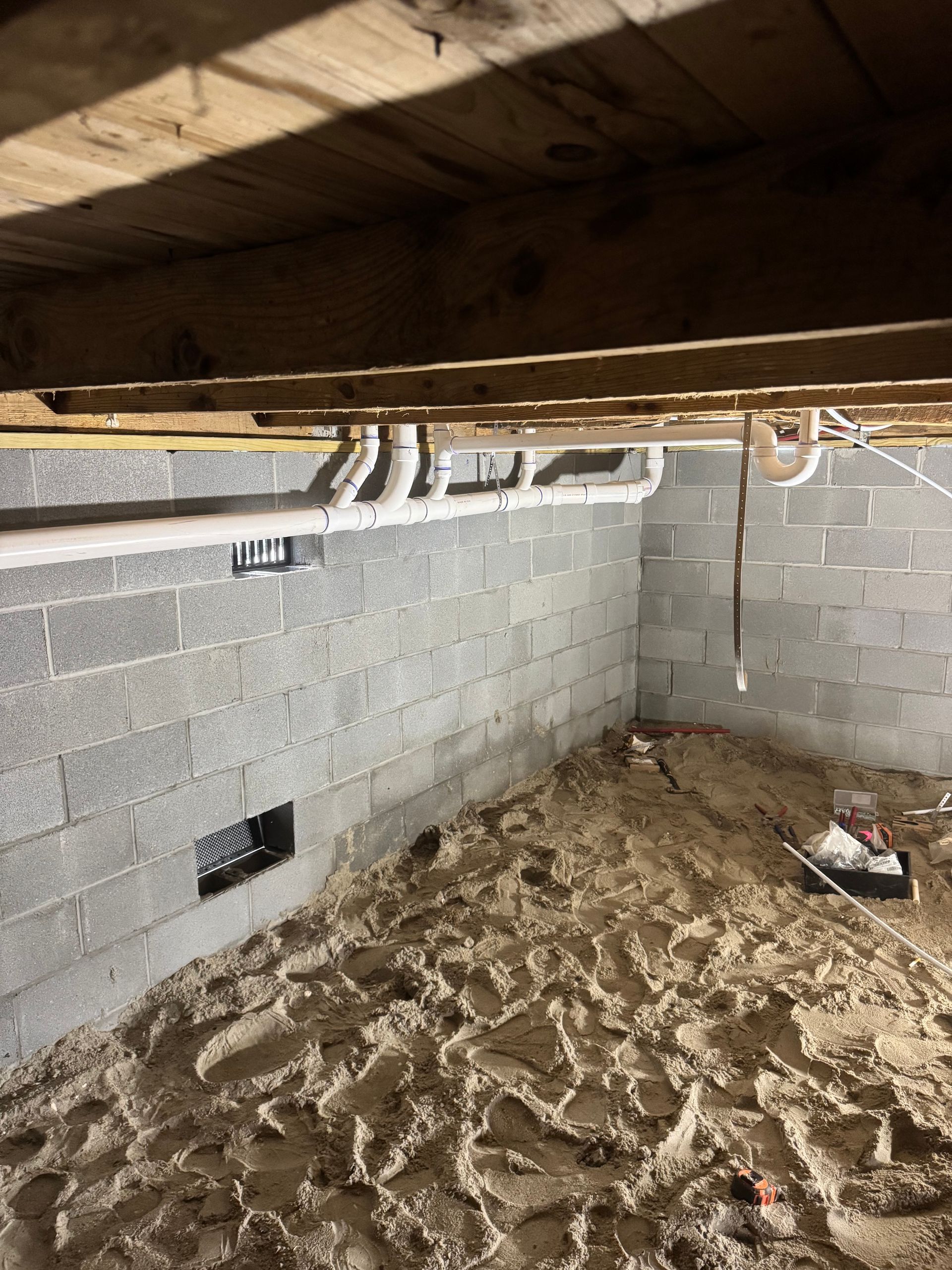 Basement with cinder block walls, exposed pipes, and a dirt floor.