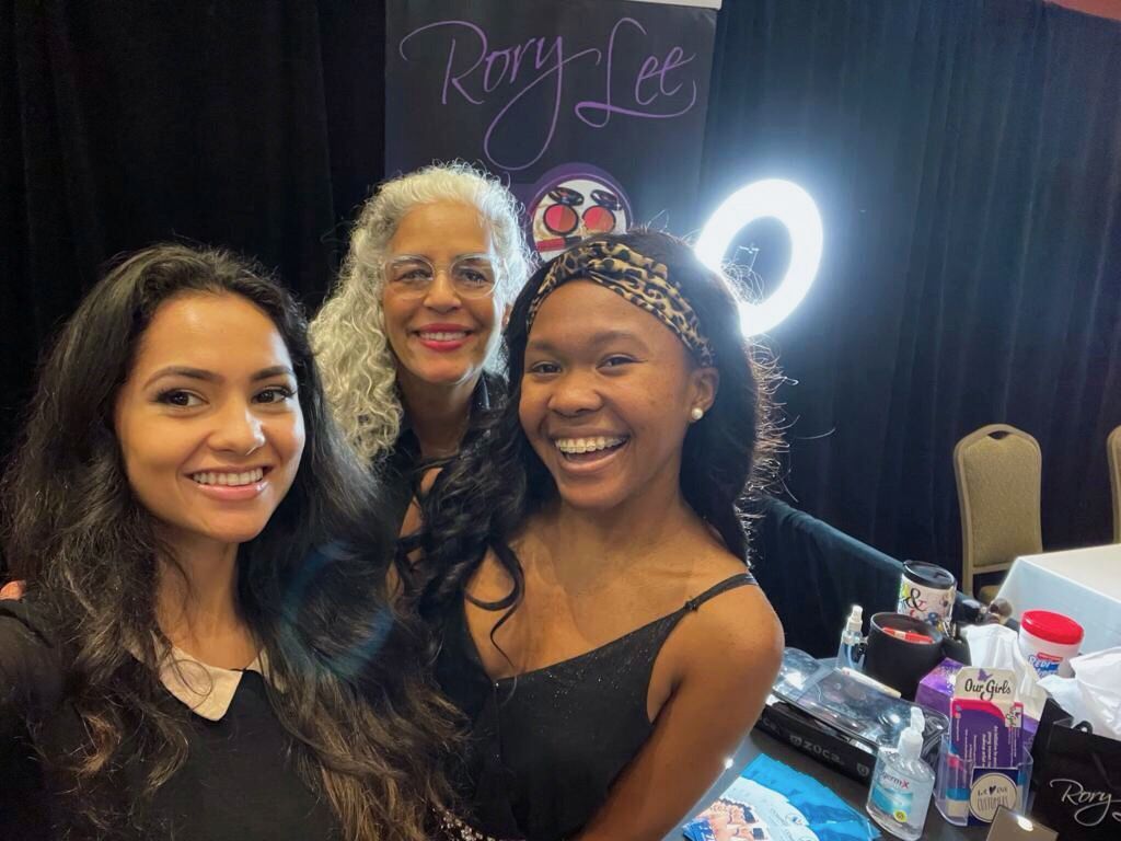 Three women are posing for a picture in front of a sign that says Rory Lee