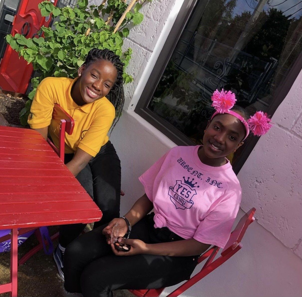 Two young girls  sit at a table with one wearing a pink shirt that says pacific nyc