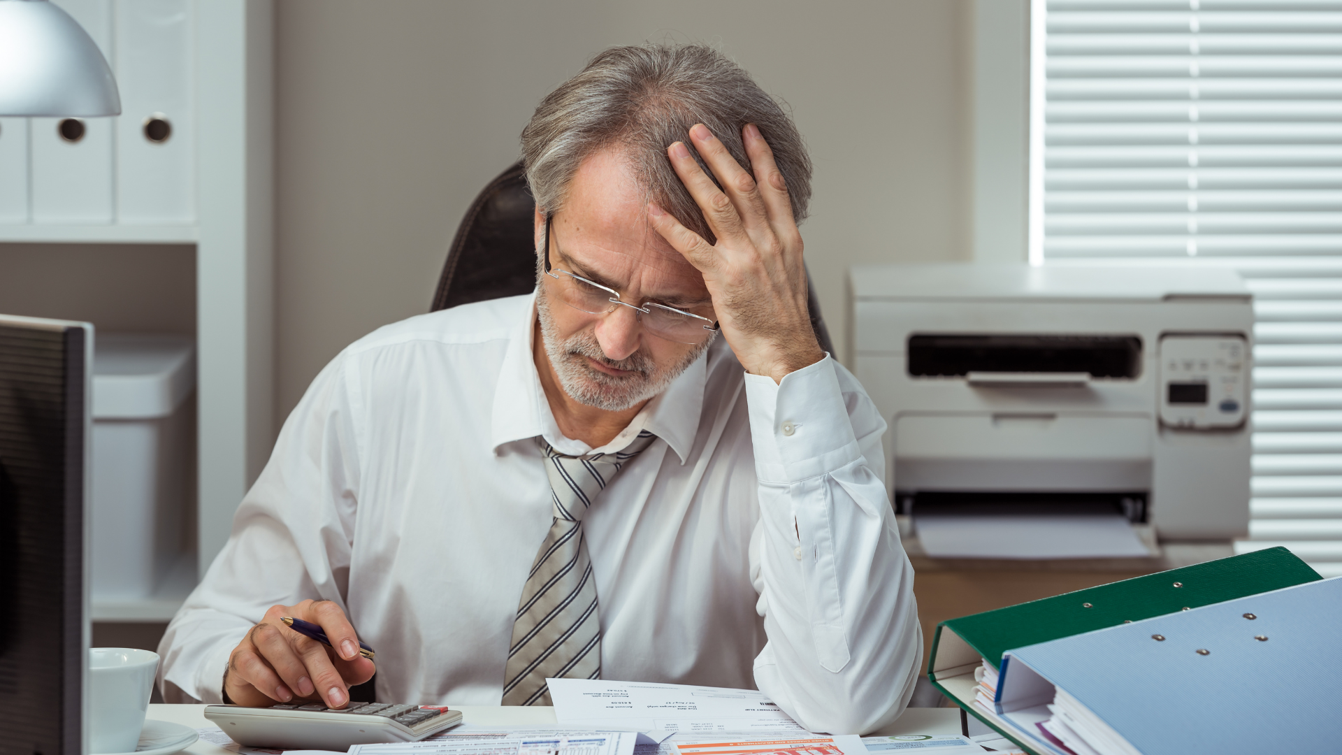 A man is sitting at a desk using a calculator and a pen.